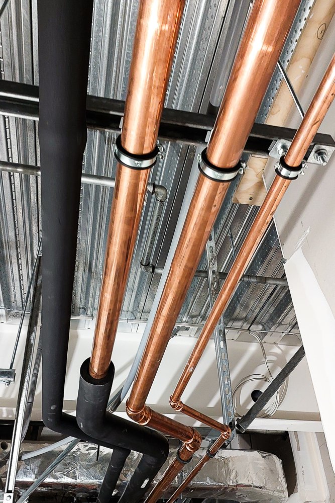 Close up of copper pipe running along the roof hung up with Flamco clips.