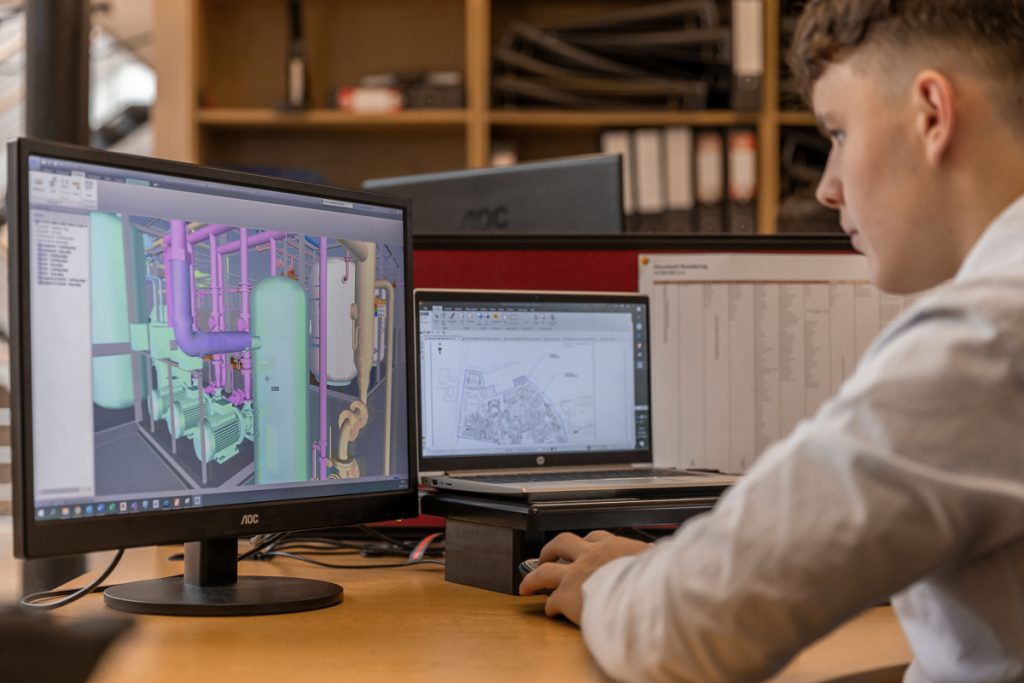 Stainless Steel - Engineering Man sitting at desk looking at computer screen that has a 3D model of pipework.